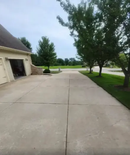 Long concrete driveway leading to a garage with trees alongside