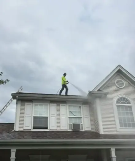 Worker in a yellow shirt spraying the roof of a white house